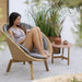 Boxhill's Twist outdoor round coffee table in beige color with teak base, with a woman sitting on outdoor lounge chair
