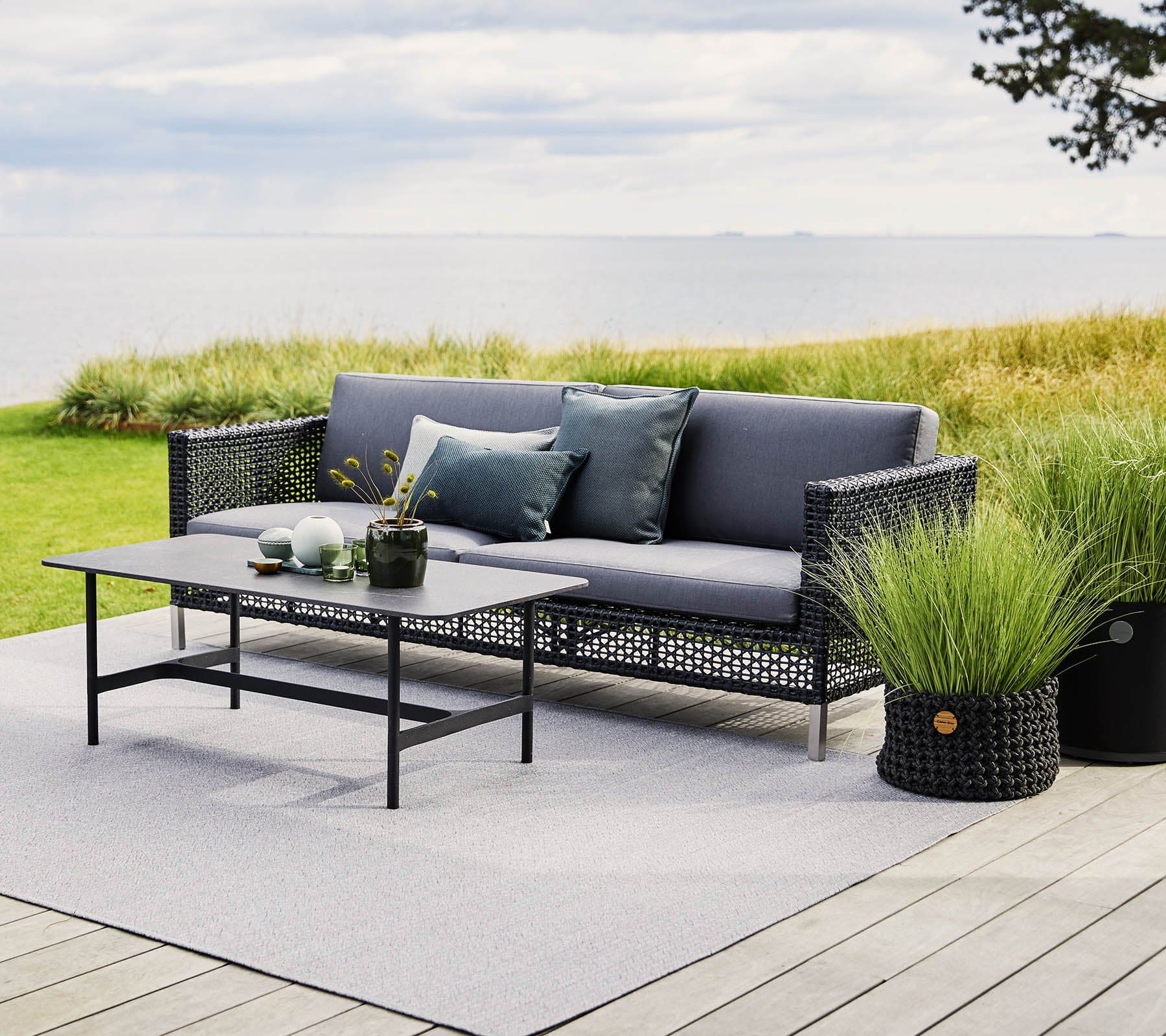 Boxhill's Twist dark grey rectangular outdoor coffee table with dark grey sofa placed on wooden platform beside grassy field