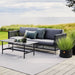 Boxhill's Twist dark grey rectangular outdoor coffee table with dark grey sofa placed on wooden platform beside grassy field