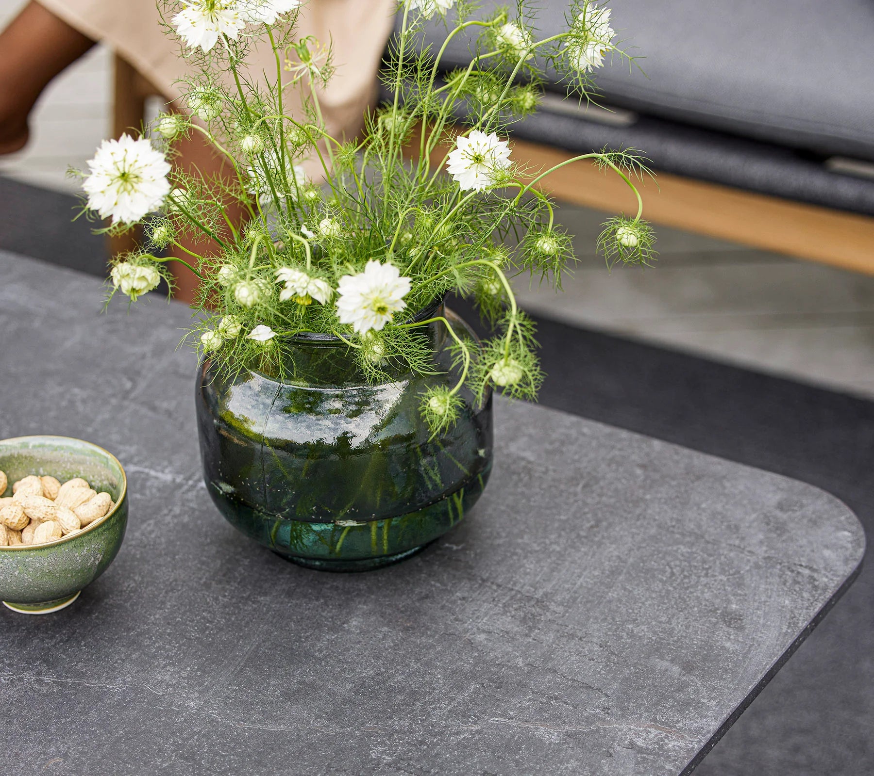 Boxhill's Twist dark grey rectangular outdoor coffee table with flowers in a green vase and cup with peanuts on top of it