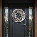 White ruffled lacquer wreath on a dark modern front door with glass side panels and wood accents.
