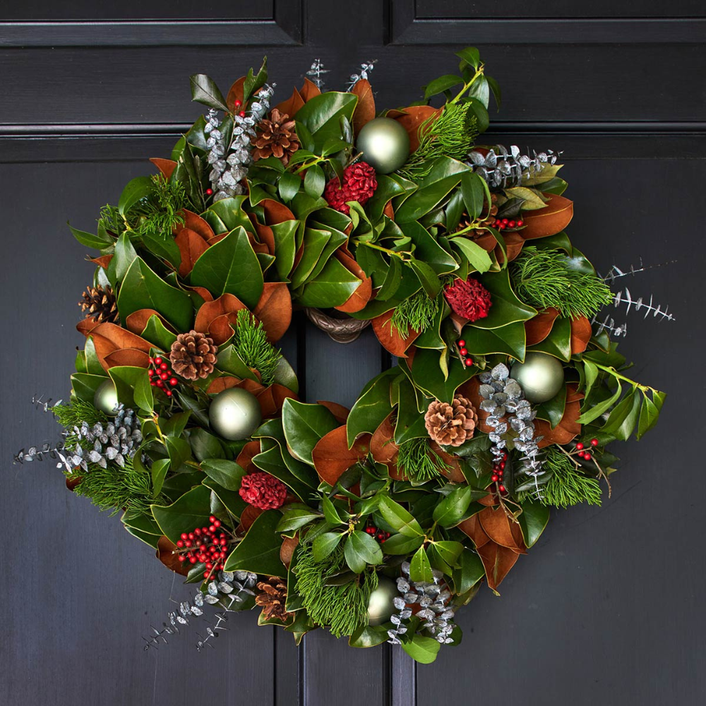 Decorative wreath with greenery, berries, and ornaments on a dark surface