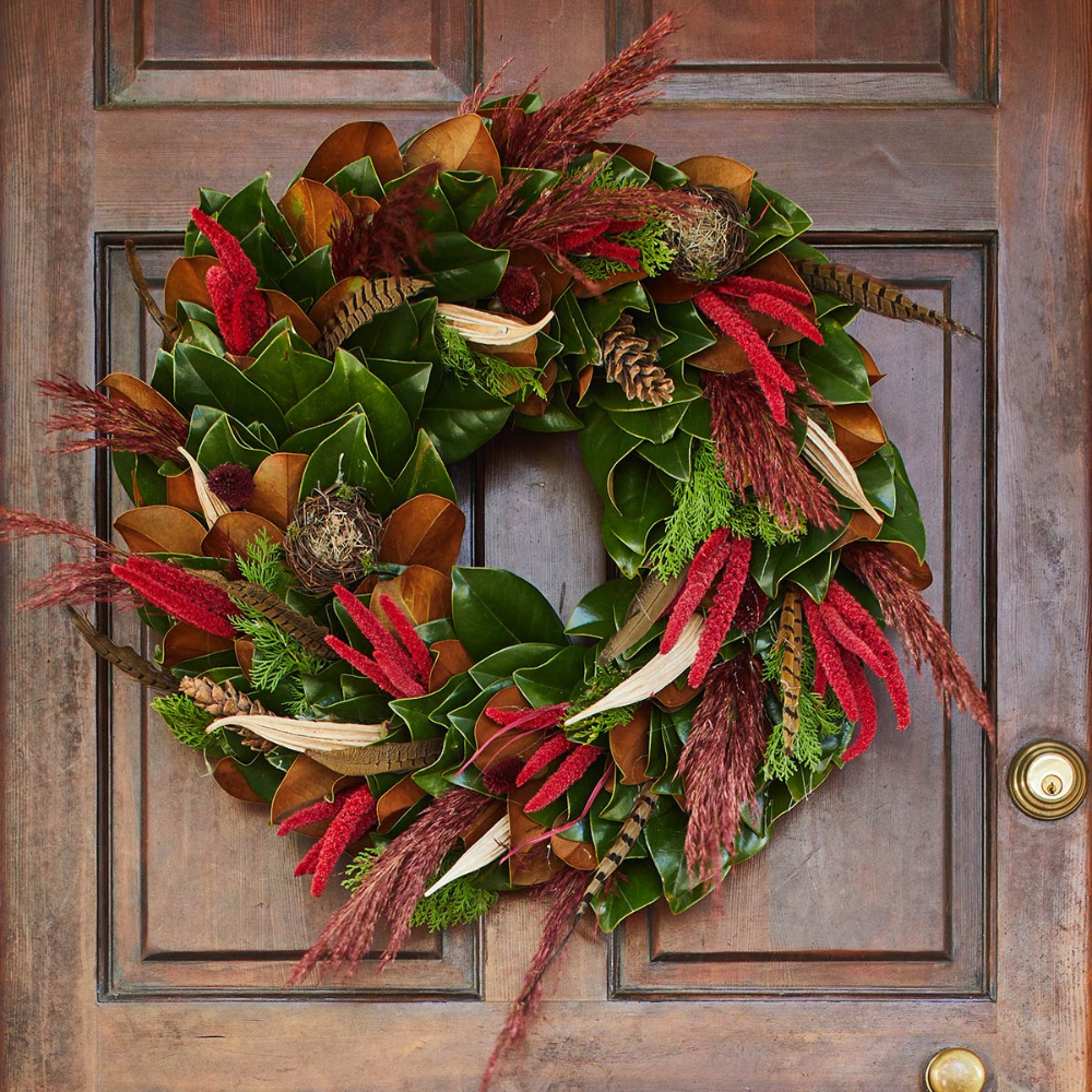 Decorative wreath with green leaves, red and brown feathers on a wooden door.