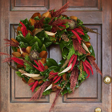 Decorative wreath with green leaves, red and brown feathers on a wooden door.