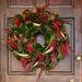 Decorative wreath with green leaves, red and brown feathers on a wooden door.