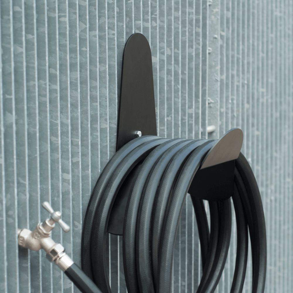 Coiled black garden hose with a metallic nozzle against a textured wall.