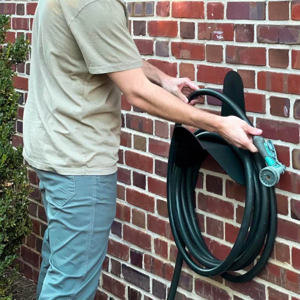 Person holding a coiled garden hose against a brick wall