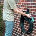 Person holding a coiled garden hose against a brick wall