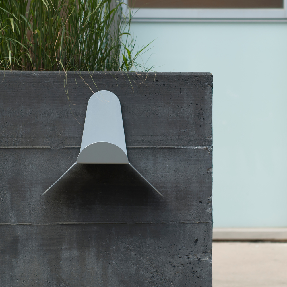 Modern outdoor light fixture on a concrete wall with plants in the background