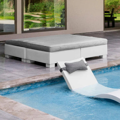 Poolside with a modern white sunbed on tiled flooring and a white in-pool chaise lounger with a gray headrest, partially submerged.