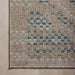 Close-up of a woven outdoor rug corner showing a textured beige base with a geometric pattern in teal blue and off-white.