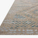 A close-up of a woven area outdoor rug with a textured, abstract geometric pattern in beige, brown, and muted blue.