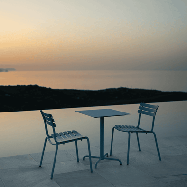 2 blue armless stackable outdoor dining chairs and a square blue dining set beside the pool