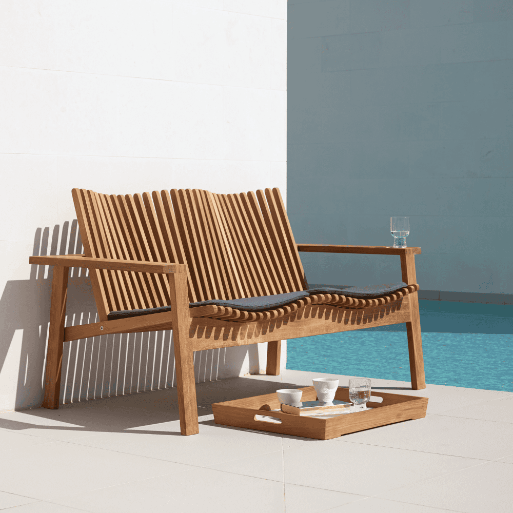 Boxhill's Amaze 2-Seater Teak Sofa lifestyle image with cushion beside the pool