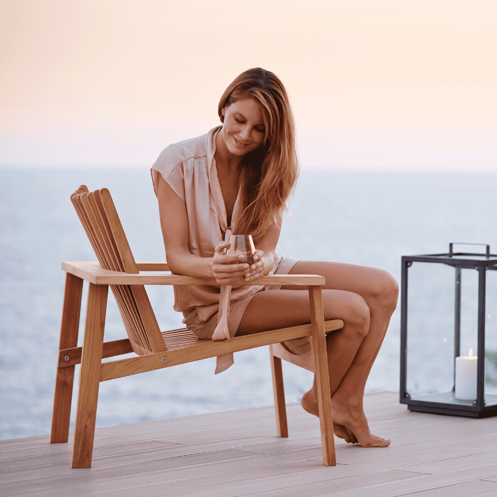 Boxhill's Amaze Stackable Lounge Teak Chair lifestyle image with woman sitting down