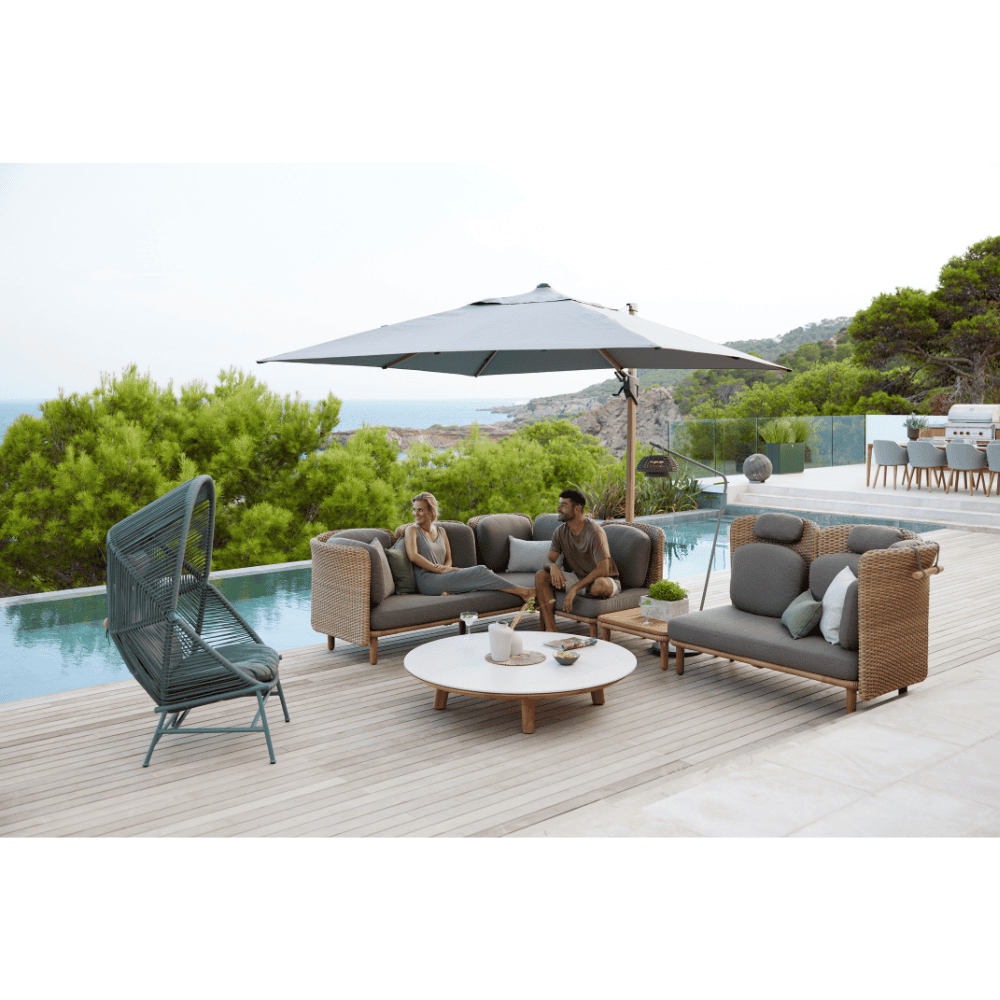 Boxhill's Arch Outdoor Coffee Table w/ Teak Table Top lifestyle image in between Arch Outdoor Sofa  with man and woman sitting down