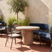 Outdoor patio furniture set featuring a round concrete-top table, black metal chairs with striped cushions, and a curved navy blue cushioned bench on a terracotta tile patio.