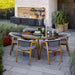 Boxhill's Aspect Teak Round Dining Table Clear Glass | Smokey Black lifestyle image with dining chairs at the garden