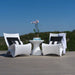 Two modern white lin-pool resin ounge chairs with black and white striped pillows, a matching white side table, and a potted orchid on a wooden deck with a green landscape and blue sky in the background.