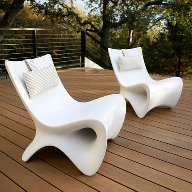 Two modern white sculptural in-pool lounge chairs on a wooden deck with trees in the background.