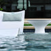 Modern outdoor furniture set in an in-pool setting, featuring a white in-pool lounge chaise with a textured light blue and white patterned throw pillow, and a matching white in-pool pedestal side table.