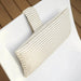 A rectangular lumbar support pillow with beige and white stripes, shown resting on a white chair in an outdoor setting with a wooden deck background.