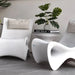 Three modern white sculptural lounge chairs arranged in a minimalist interior setting with a small round side table, potted green plant, and a book titled Gray Malin.