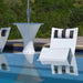 Modern outdoor poolside furniture set with a white pedestal in-pool table, white lounge chairs with black-and-white striped cushions, and a matching white lounge chair in the foreground, reflected in the blue water. Lush green foliage is visible in the background.