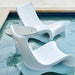 Two modern white wavy lounge chairs in a swimming pool, with a matching round ice bin in pool side table between them.