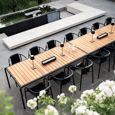 An outdoor patio with long wooden outdoor dining table with black metal frame surrounded by black outdoor dining chairs