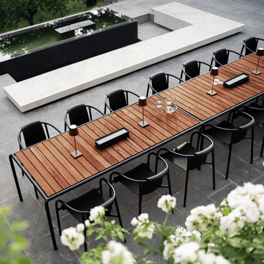 A long outdoor table set with black chairs, featuring a table lamp elegantly positioned on its surface.