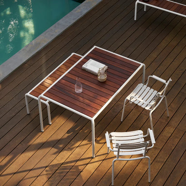 Poolside wooden deck with rectangular wooden-top dining table with white frame, matching benches, and two white chairs