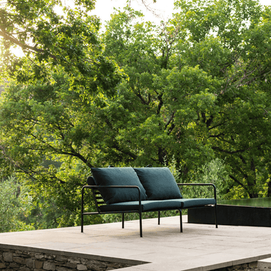 A dark green outdoor lounge 2-seater sofa with black aluminum frame set on a patio surrounded by trees