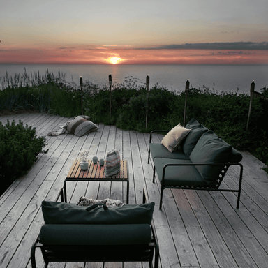 A dark green outdoor lounge 2-seater sofa with black aluminum frame and a wooden outdoor lounge table set on a wooden deck outdoor area 