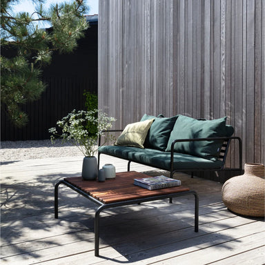Dark green outdoor loveseat with black metal frame and an outdoor coffee table, set on a wooden deck patio