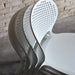 Four stacked white outdoor side chairs with perforated backrest against a beige brick wall