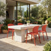 Outdoor dining with white textured rectangular concrete table surrounded by four orange dining chairs and greenery