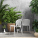 Two white armless outdoor side chairs surrounded by potted green plants in a modern patio setting