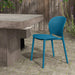 Blue armless outdoor dining chair with perforated backrest beside concrete table on patio with wooden fence and greenery