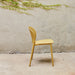 Side view of yellow outdoor side chair  against a plain concrete wall with greenery above