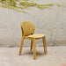 Two stacked yellow outdoor side chairs with perforated backrest against a plain wall with greenery above