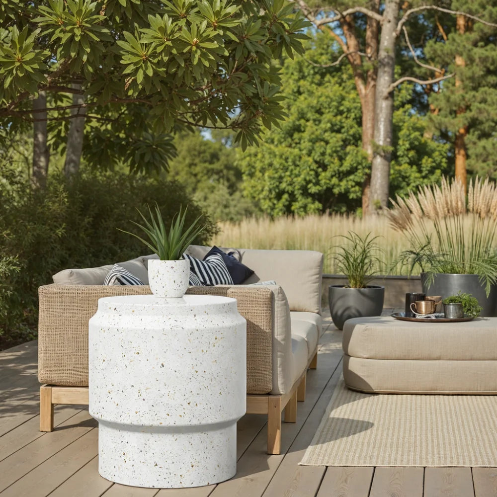 Wooden deck patio with white speckled concrete round stool table, brown wicker sofa with gray cushions, coffee table and greenery