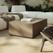 Patio seating with beige textured concrete rectangular outdoor coffee table, white sectional sofa on tiled floor, greenery
