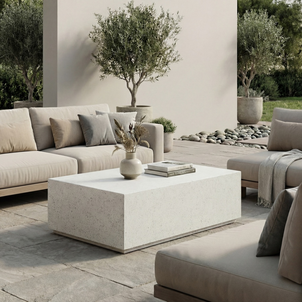 Modern patio with rectangular white concrete outdoor coffee table, beige sofa and chairs, surrounded by greenery