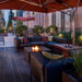 Rooftop outdoor seating area with dark brown square fire pit table, sectional sofa, and red parasols overlooking city skyline