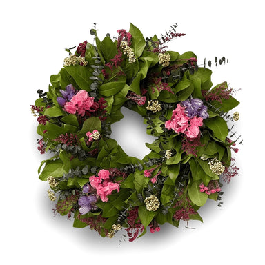 Decorative green leaf wreath with soft pink, purple, and white flowers against a white background.