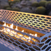 Close up view of white outdoor rectangular fire pit with geometric cut-out design with flickering flames inside over lava rocks