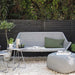 Outdoor seating area with a gray sofa, ottoman, and small table in a garden setting.