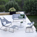 Outdoor patio set with chairs, table, and ottoman on a white patio with greenery.