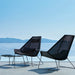 Two black outdoor chairs with a small table on a reflective surface with a mountainous background.